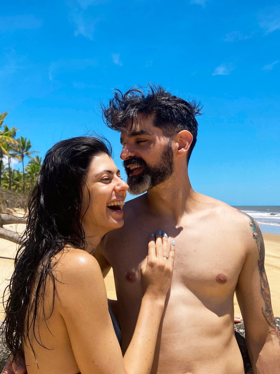 Foto dos noivos sorrindo à beira-mar